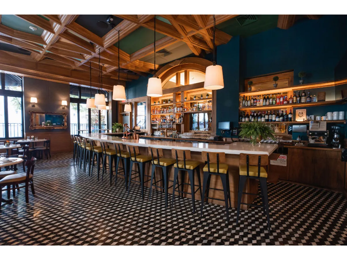This image captures Bar Alder, highlighting its lively and sophisticated atmosphere. The bar counter features an array of bottles, hanging light fixtures, and a decorative ceiling. Guests are seen socializing, enjoying drinks, and dining, reflecting the energy and vibrancy of the hotel's on-site culinary scene.