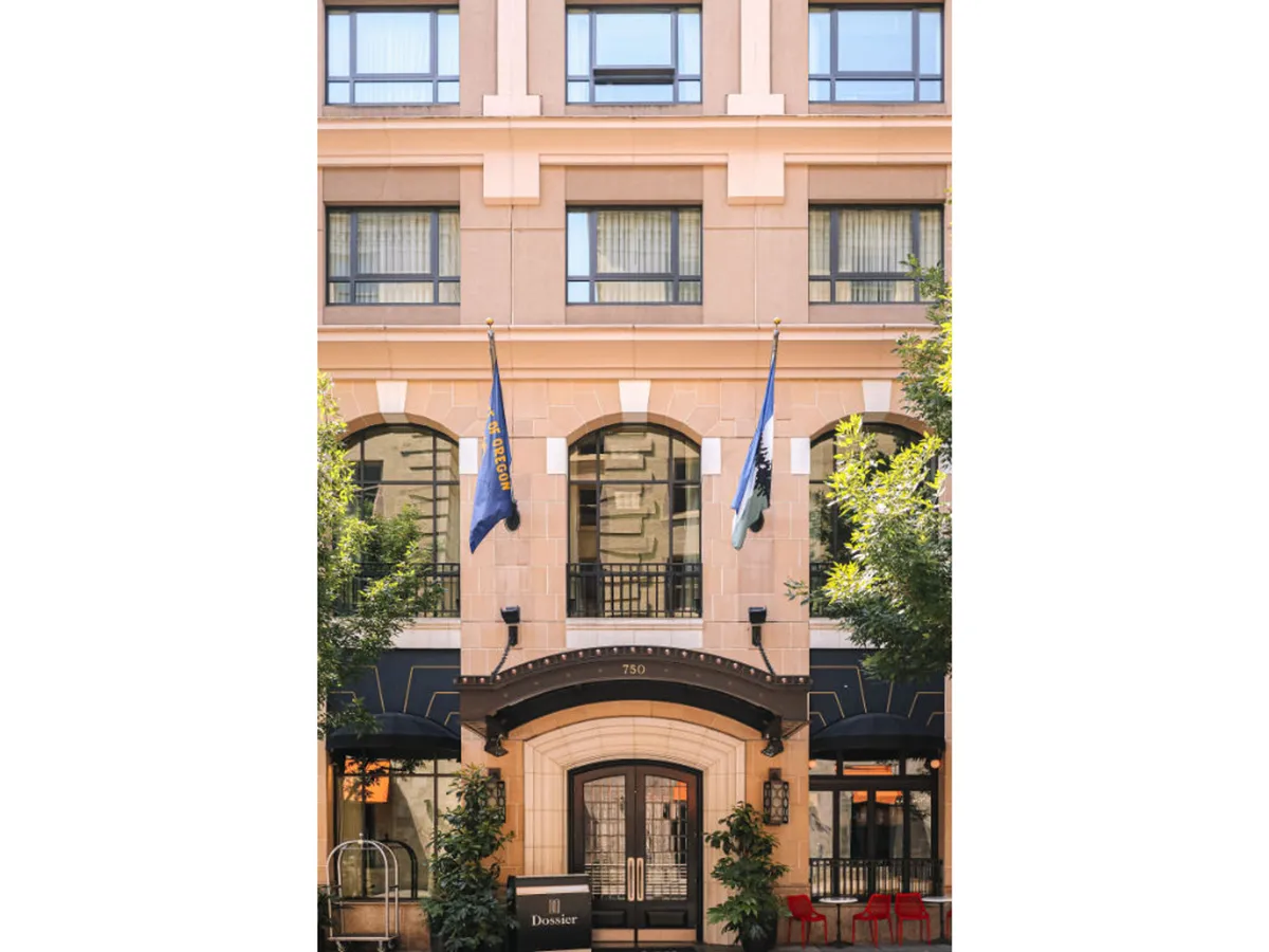 This exterior shot captures the hotel’s grand entrance, featuring an arched doorway, decorative flags, and landscaped surroundings. The scene invites the viewer to imagine arriving at the center of Portland’s bustling downtown, with hints of street life and the city’s energy just beyond the doors.