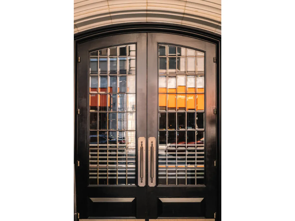 This exterior image shows the building's welcoming double doors with large glass panels and metal handles, offering a clear, accessible entryway from the street. The design is modern and inviting, providing a sense of easy transition for all guests, including those with mobility devices.