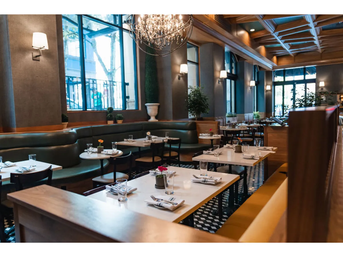 A sophisticated yet relaxed dining space featuring a chandelier, an abundance of greenery, tables adorned with floral arrangements, and comfortable booth seating. The environment is both intimate and inviting, suggesting moments of rest and sociability.