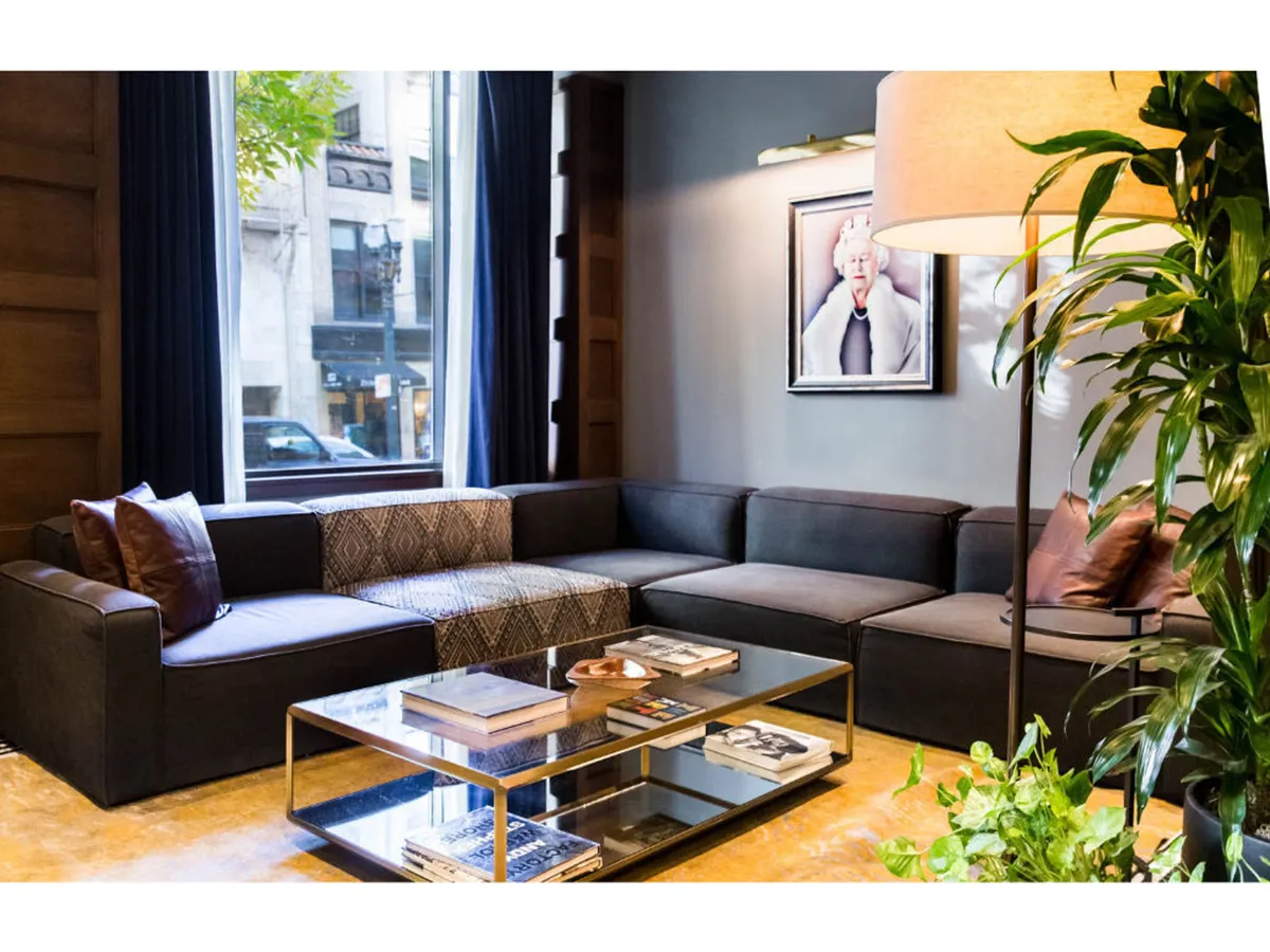 A cozy lounge area featuring a plush sofa, coffee table, artwork, and city views through a large window. The scene invites guests to relax, socialize, or enjoy quiet moments, showcasing the comfort and privacy of the suite experience.