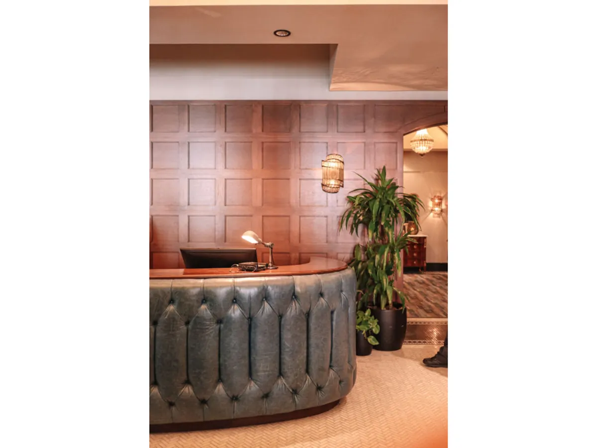 The elegant hotel reception area with a curved desk, wood paneling, and modern hanging light fixtures. A staff member welcomes guests, and the overall mood is inviting and sophisticated, emphasizing the ease of check-in and professional service.